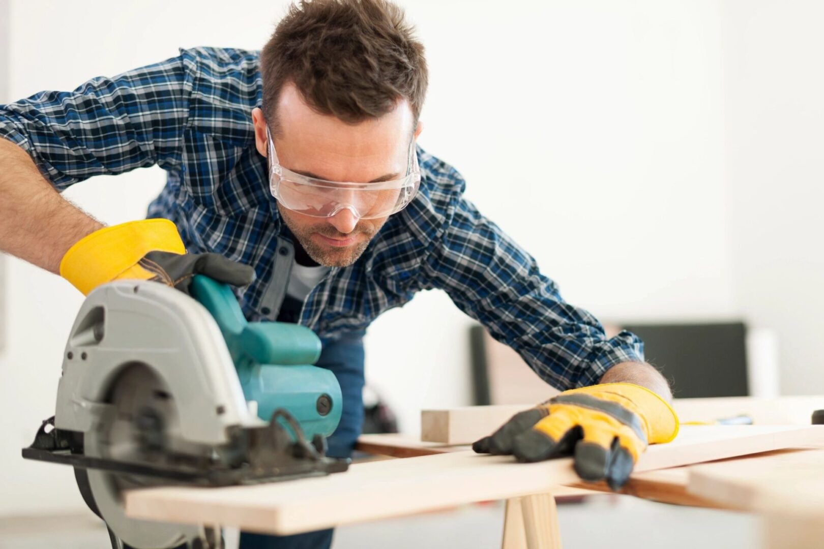 A man wearing safety glasses and gloves using a circular saw.