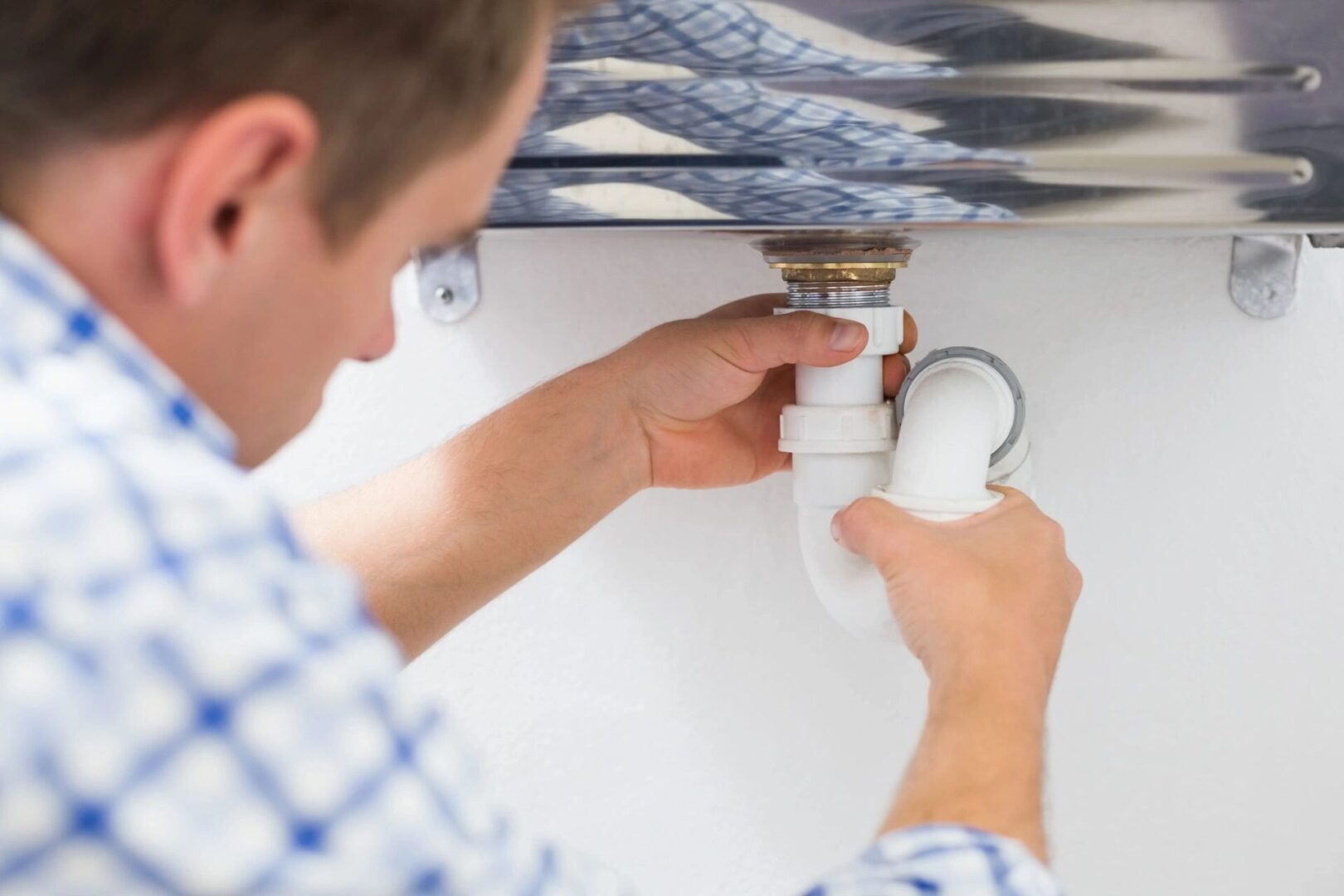 A man fixing the faucet of a kitchen sink.