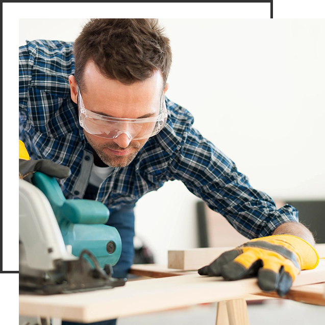 A man wearing safety glasses and gloves working on wood.